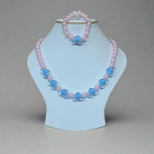 Necklace with pink and blue beads on a light blue stand against a green leafy background