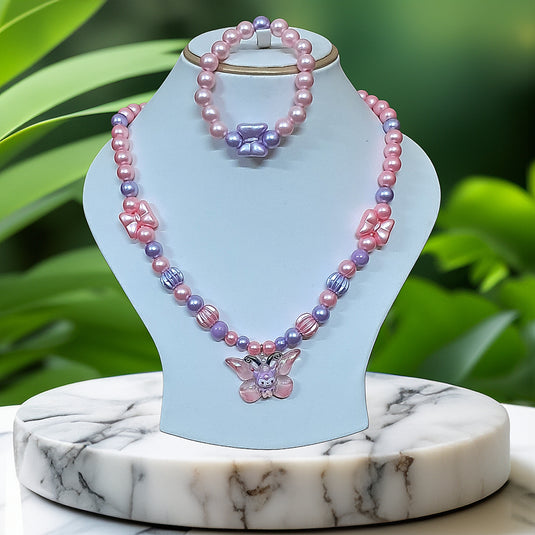 Pink and purple beaded necklace with butterfly pendant on a light blue stand against a green leafy background.