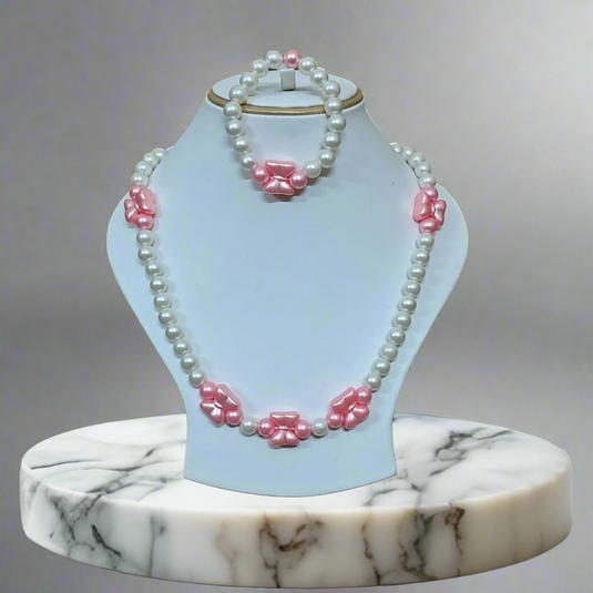 Pearl necklace with pink floral accents on a white stand against a green leafy background