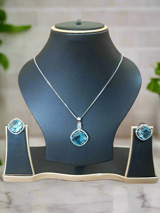 Aqua Blue Pendant Set by Garimas featuring CZ studs and silver-plated chain displayed on a jewelry stand.