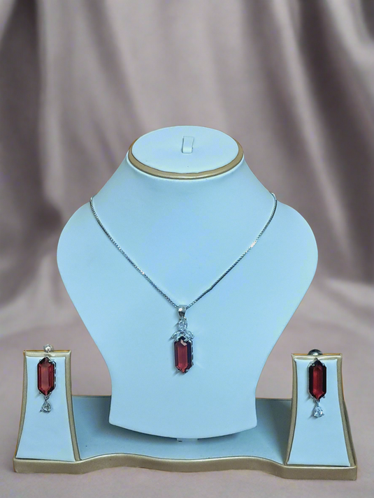 Elegant Garimas pendant set featuring red ruby and CZ stones on a silver-plated chain, showcased on a jewelry display.