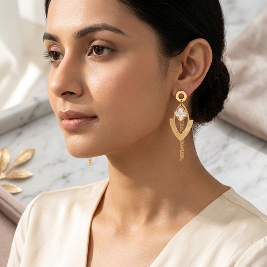Woman wearing a gold-tone quatrefoil drop earring with a textured V-shaped pendant and chain tassels