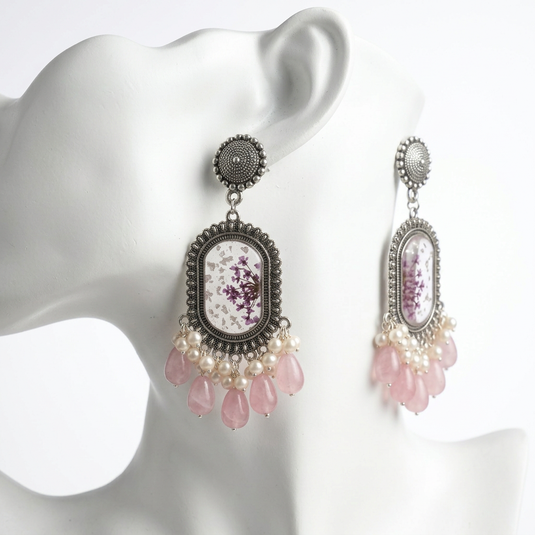 GARIMAS blush pink floral resin drop earrings displayed on a white mannequin, showing silver-tone frames and pink teardrop dangles.