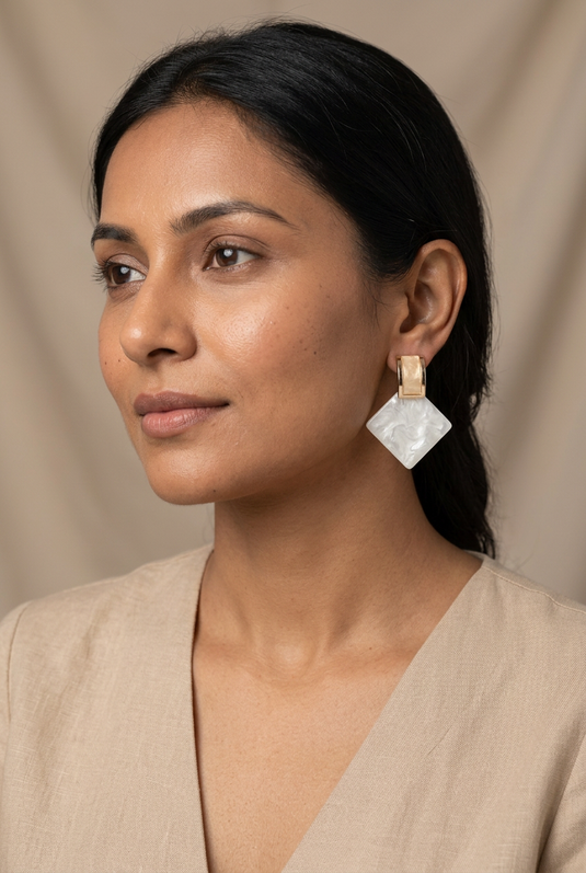 GARIMAS ivory marble-effect square drop earrings worn with a beige blouse, featuring champagne-coloured gold-tone tops.